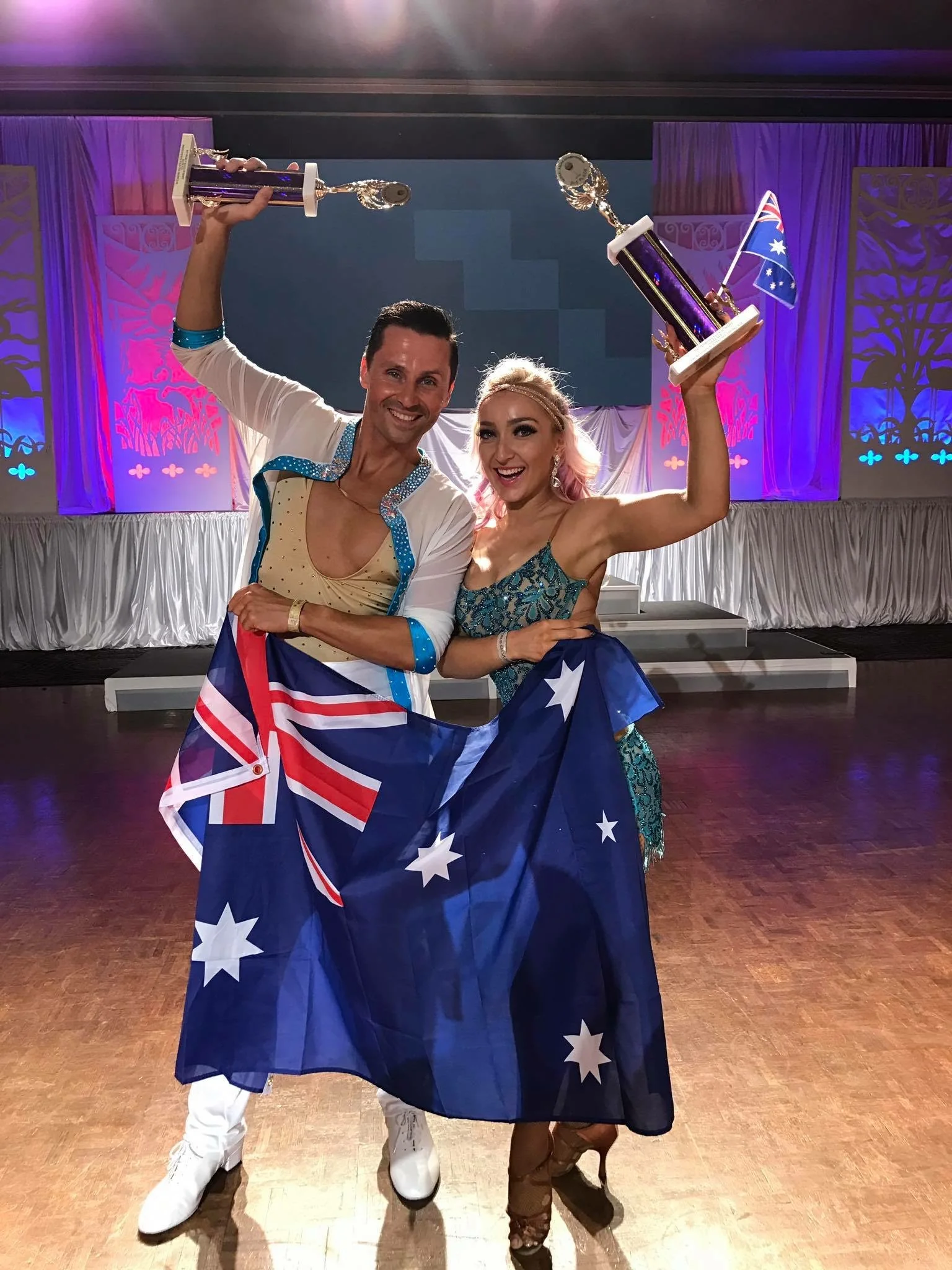 Kristi Hall celebrating an international Latin dance championship with trophies and the Australian flag